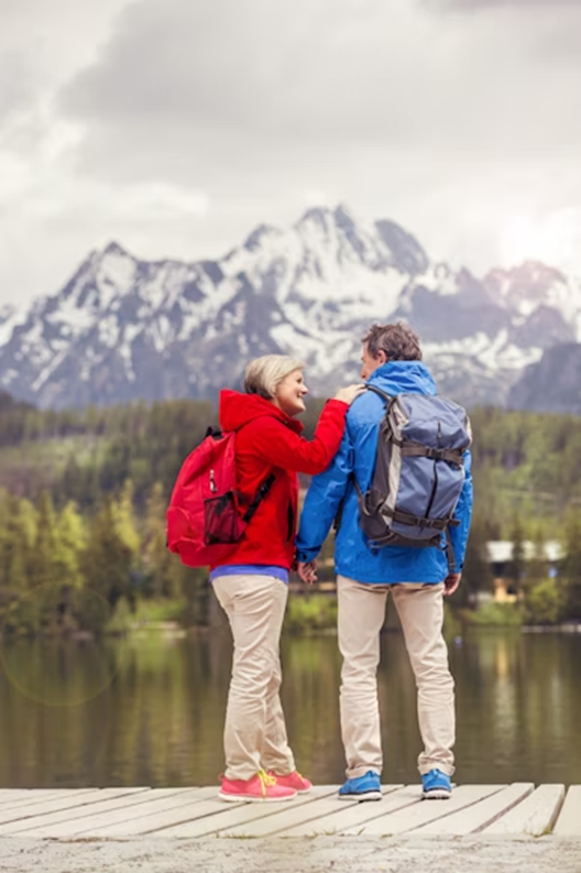 Elderly woman climbing rocks with support from her partner in a scenic outdoor setting.